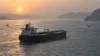 An unbranded oil tanker transiting a narrow sea lane at sunrise with two patrol craft in the distance
