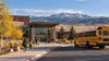 Editorial illustration of a generic public school campus and unbranded school bus in a small Wyoming community.