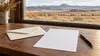 AI-generated editorial illustration of a blank sheet, plain envelope and pen on a desk overlooking high-plains grassland; not an actual ballot, polling site or voting event.