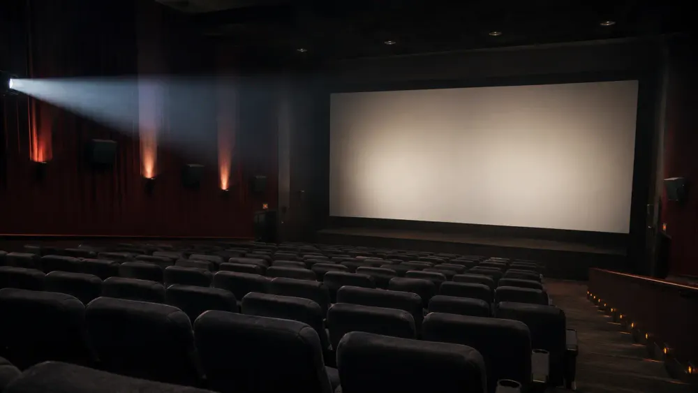 Empty movie theater with projector light crossing a dark auditorium toward a blank screen.