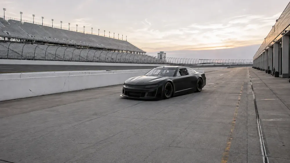 An unbranded stock car parked in an empty speedway pit lane at dawn