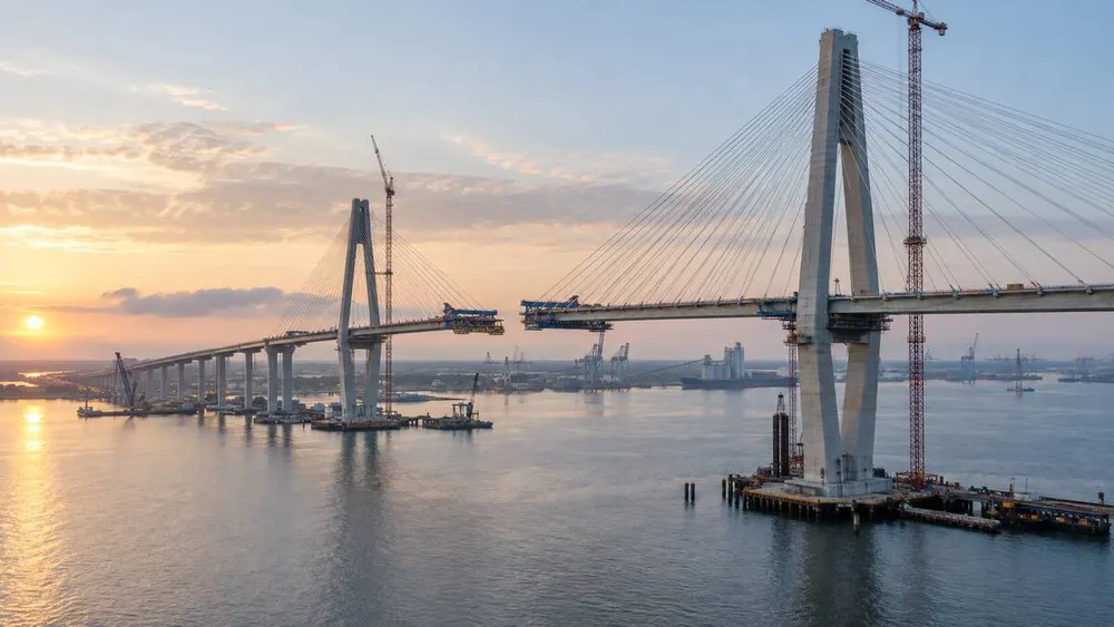 Editorial visualization of a cable-stayed bridge under construction across Mobile Bay at sunrise
