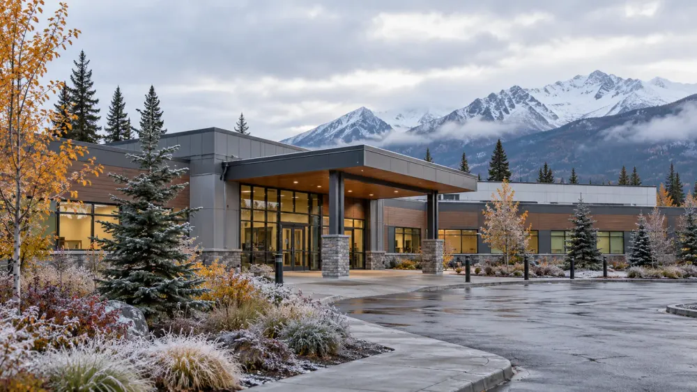 A modern Alaska community health clinic beneath mountains in cool early-autumn weather.