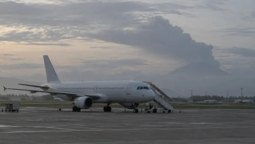 An unbranded passenger aircraft on a tropical airport apron with a distant volcanic ash plume