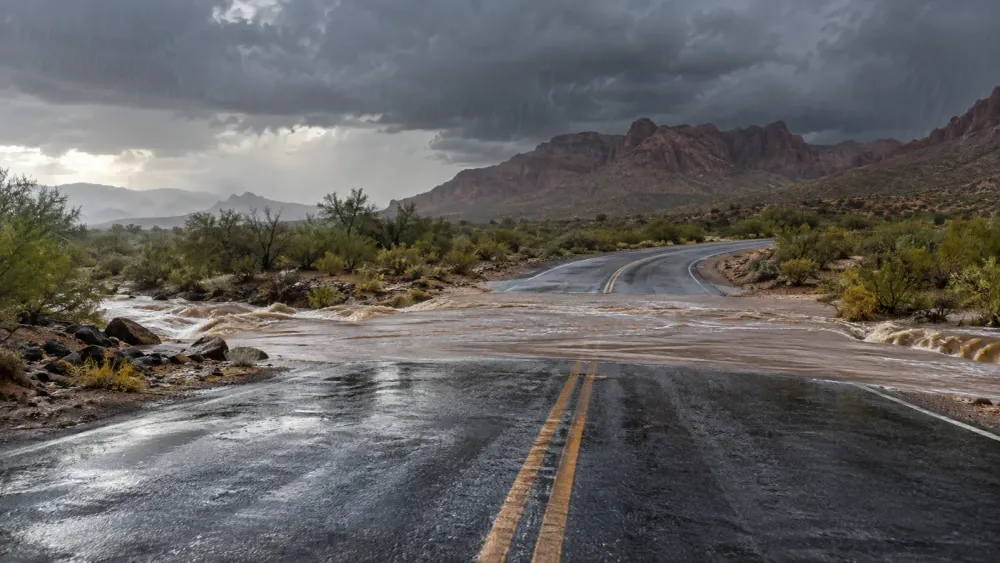 Monsoon rain sending muddy water across an empty desert highway beneath dark clouds in Arizona