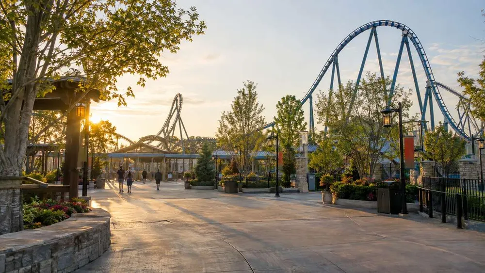 A quiet amusement-park plaza with modern steel roller-coaster track in warm morning light.
