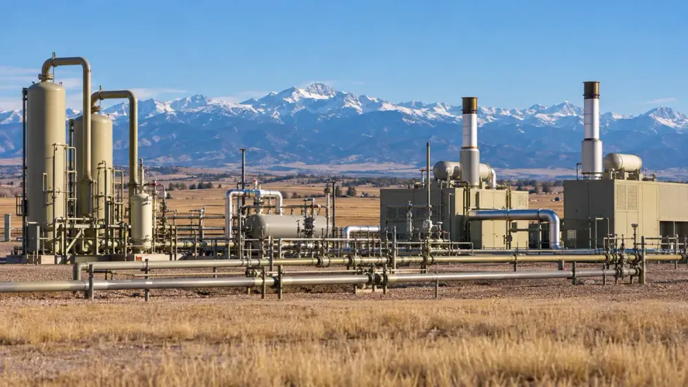 Oil and gas processing equipment on Colorado's eastern plains with the snow-covered Front Range in the distance.