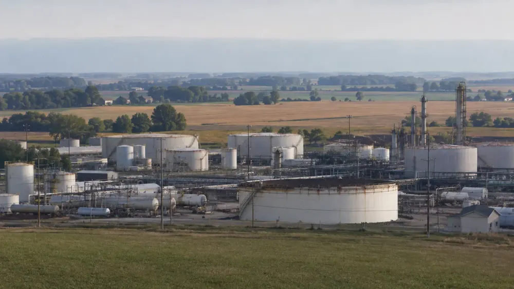 Unbranded regional fuel refinery and storage tanks beside Midwestern farmland in soft morning light
