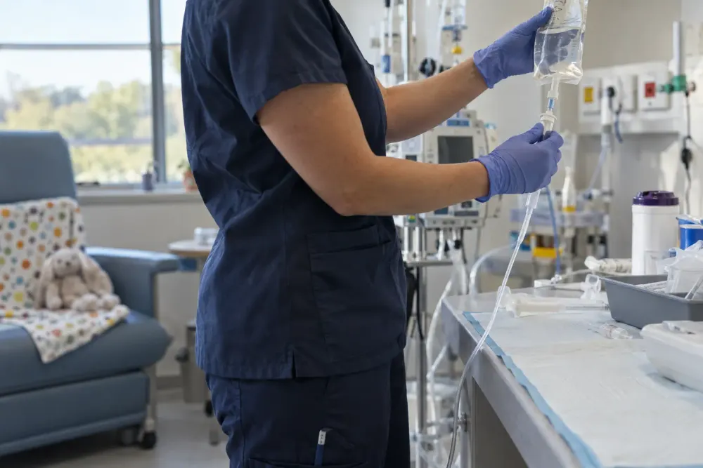 A pediatric clinician prepares an intravenous infusion in a hospital treatment room.