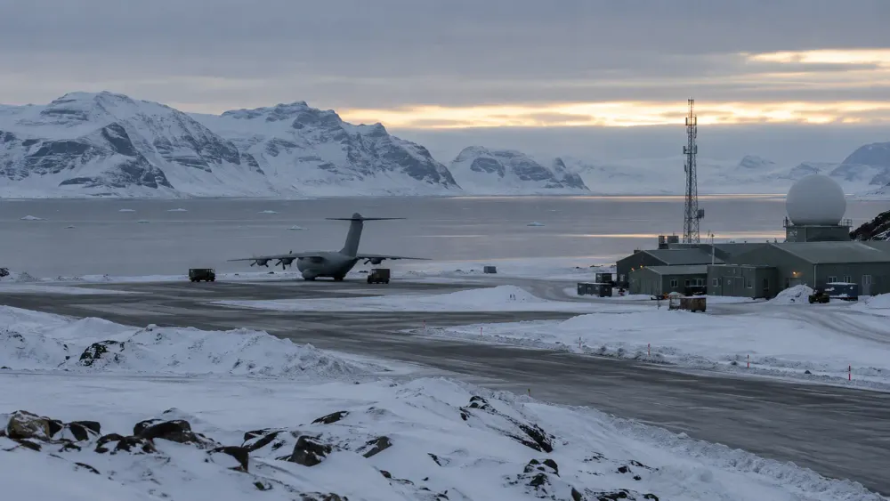 A generic Arctic military airfield beside a frozen fjord, with an unmarked transport aircraft, radar dome and communications tower.