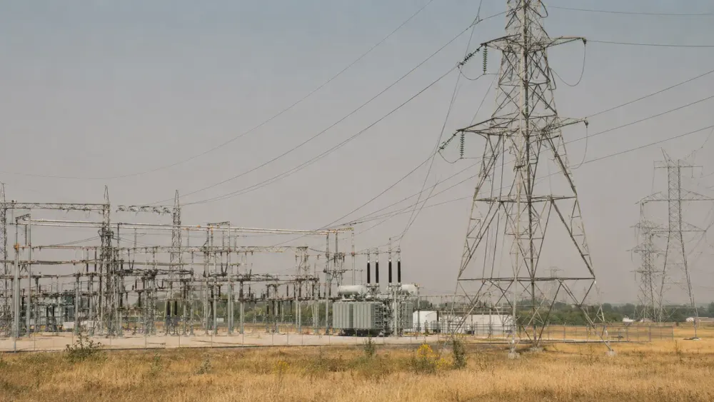 Electrical transmission towers and a large substation under hazy late-summer heat in the United States