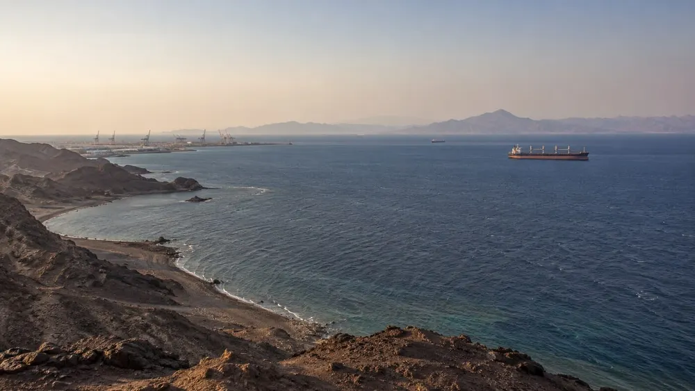 Commercial cargo vessels traveling off an arid Red Sea coastline near the Bab el-Mandeb approach