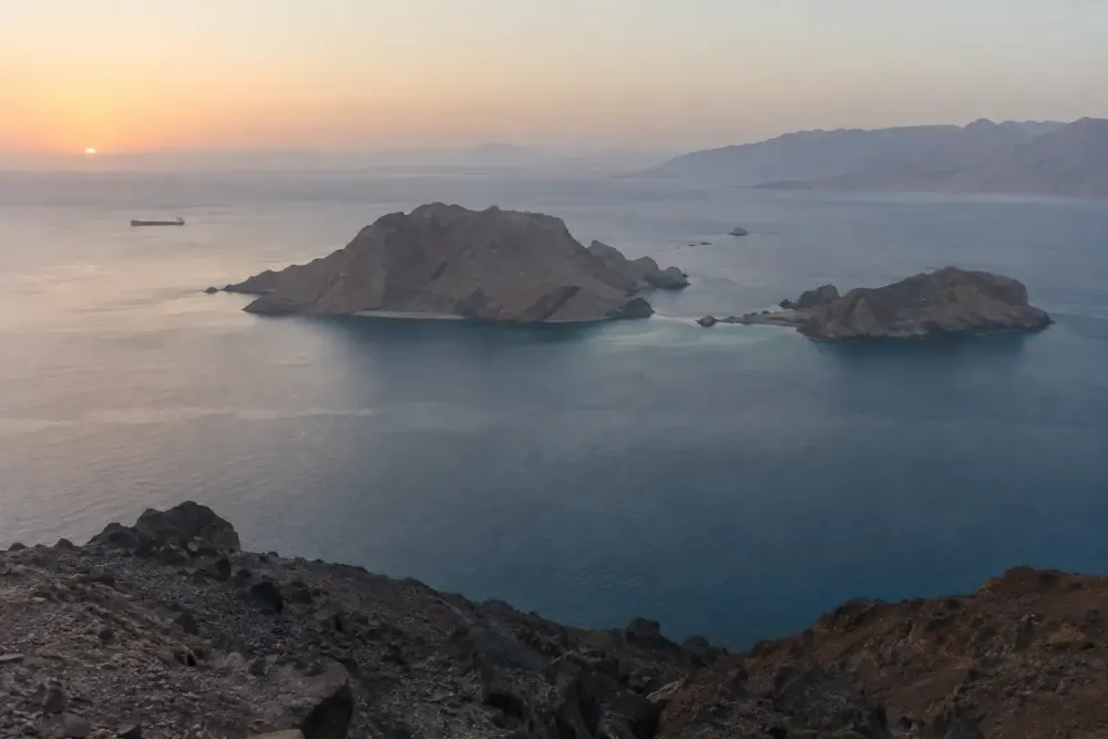 Arid Red Sea islands surrounded by calm blue water with a distant cargo vessel at dawn