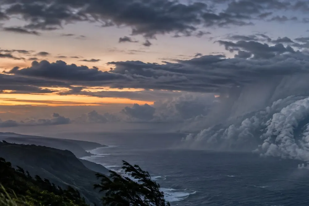Dark rain bands over rough ocean near a wind-swept Hawaiʻi coastline before dawn