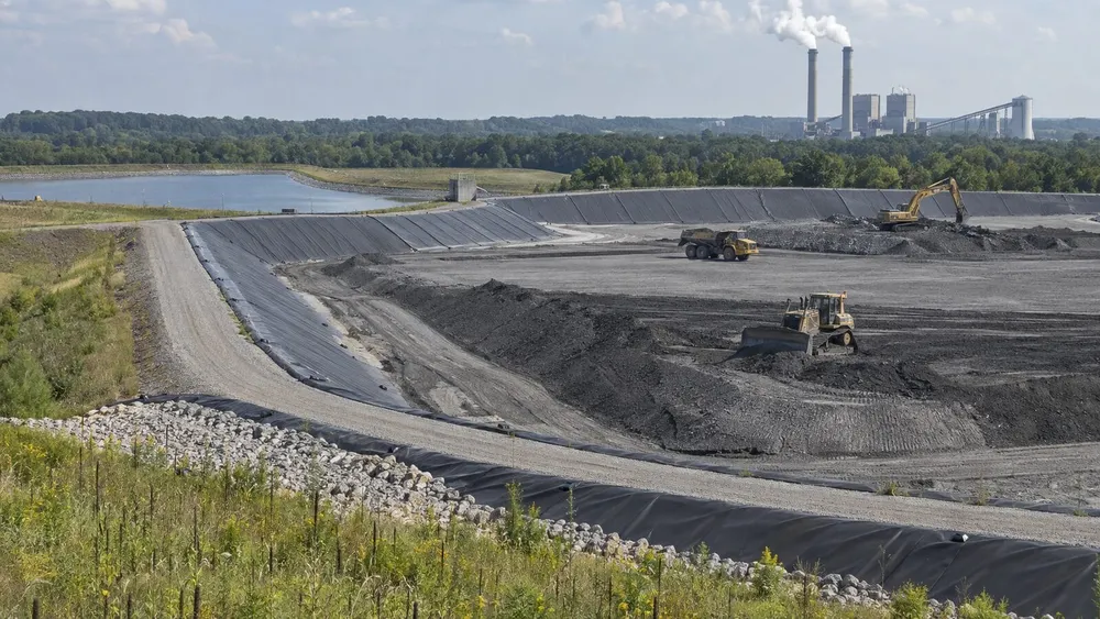 Lined industrial coal-ash impoundment with earth-moving equipment and a distant power plant