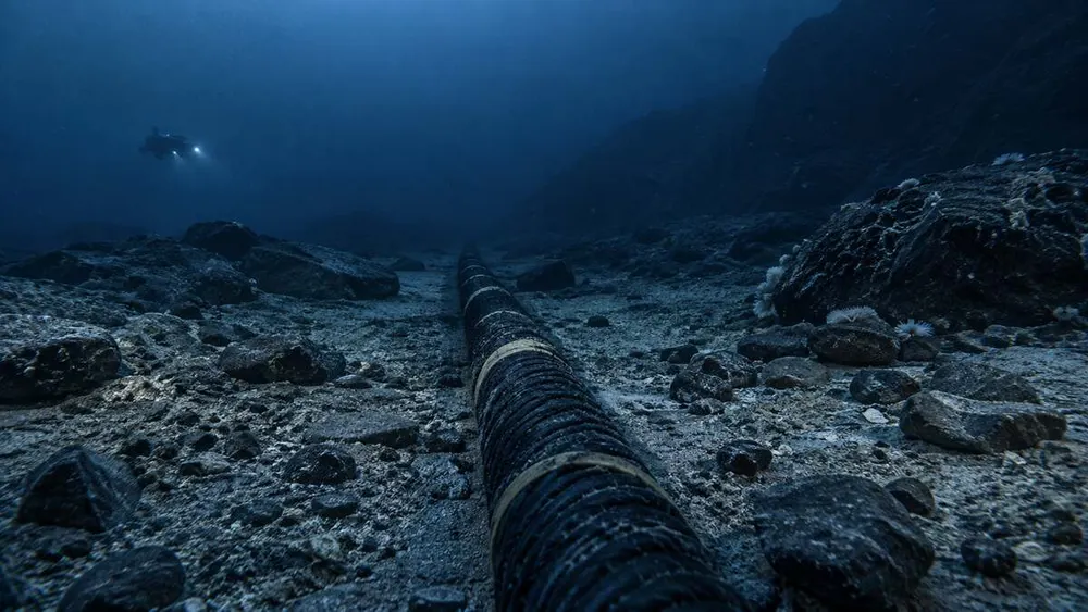 A symbolic armored communications cable crosses a cold Arctic seabed while a distant unmarked research submersible observes.