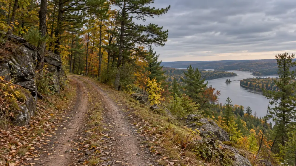 A narrow unpaved road follows a wooded bluff above a river in Minnesota in early autumn.
