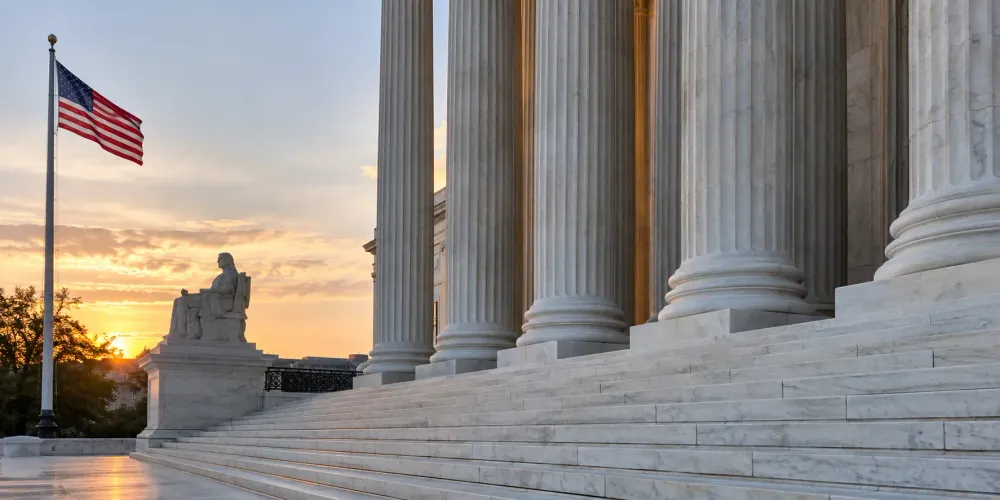 The U.S. Supreme Court’s stone columns and steps beside an American flag at sunrise