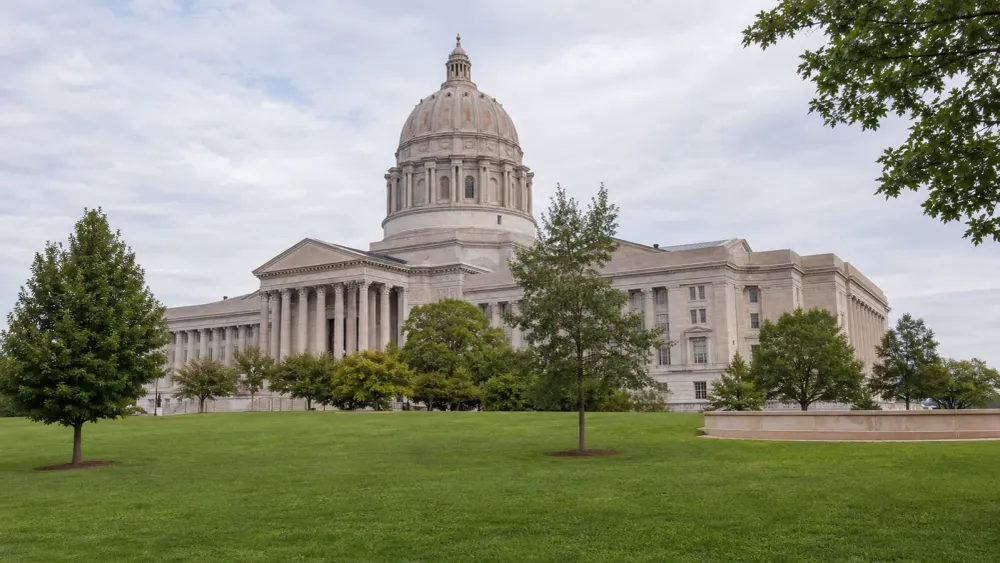 A distant view of the Missouri State Capitol across a green lawn in soft morning daylight