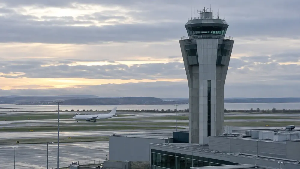 Unbranded airport control tower beside runways and a taxiing passenger aircraft at dawn.