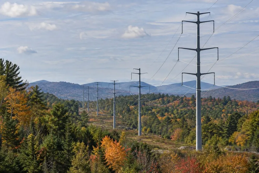 Steel transmission monopoles cross a wooded New Hampshire landscape in early autumn.