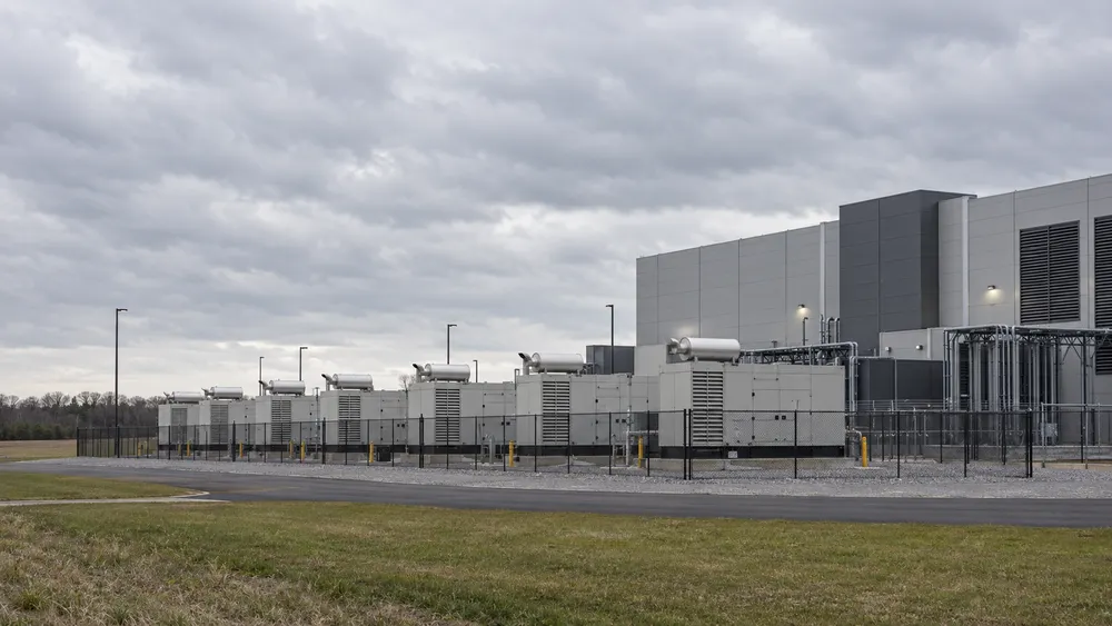 A generic modern data center with enclosed generator units behind a low fence under an overcast sky.