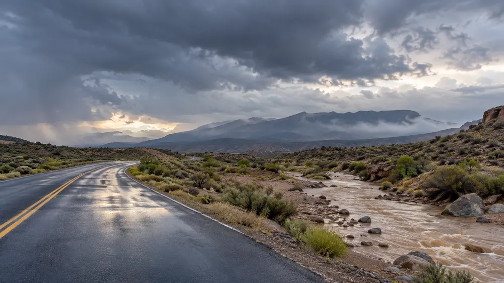 Storm clouds over a rain-soaked New Mexico road beside a flowing desert arroyo.