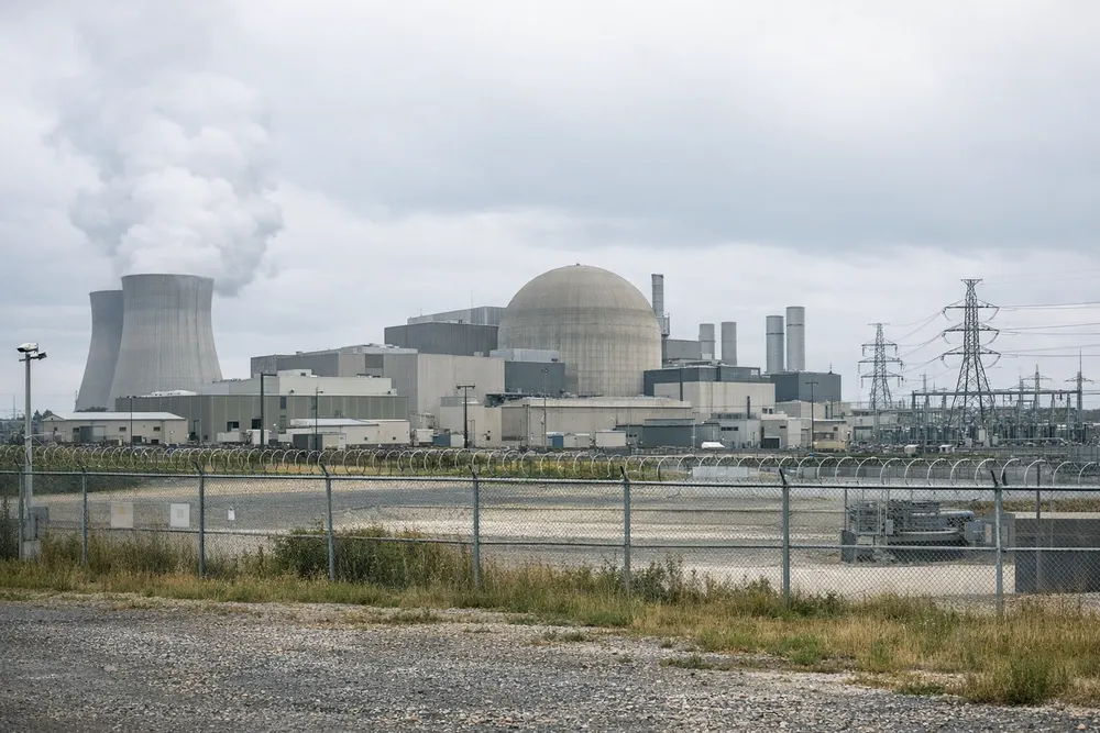 Generic distant view of a secured industrial nuclear research complex under an overcast sky, with utility buildings and infrastructure but no identifiable signs or people.