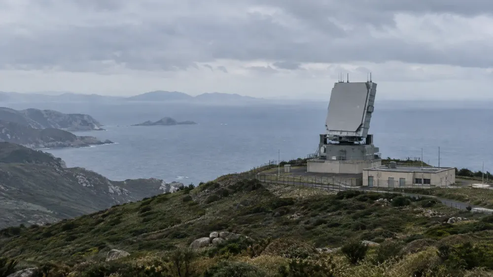 Coastal air-defense radar installation overlooking the sea under an overcast sky.