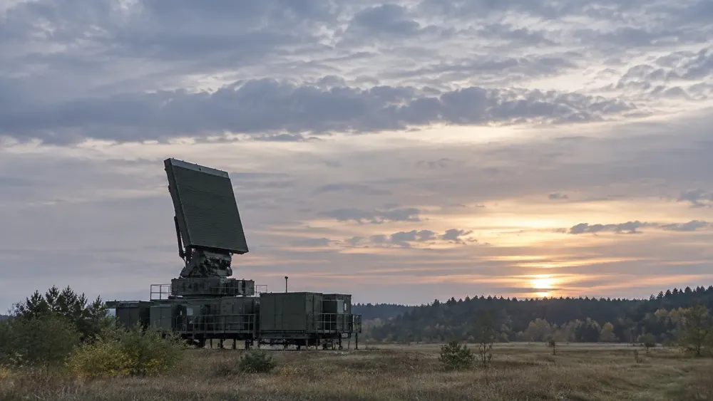 A ground-based air-surveillance radar scans the sky over a flat northern European field at dawn.