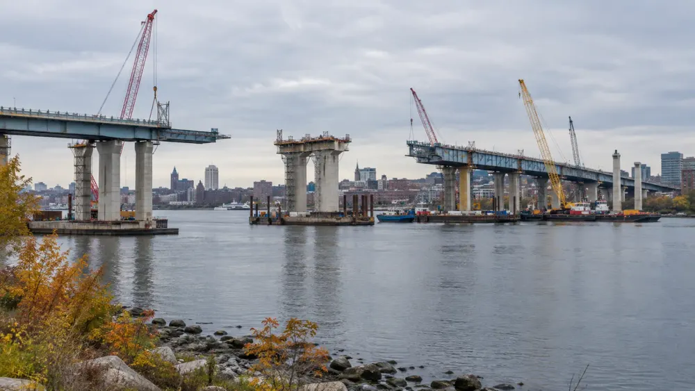 Editorial illustration of a major bridge replacement under construction across an urban river.