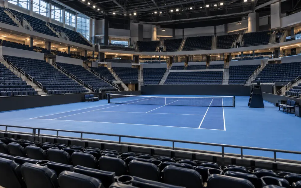 An empty blue tennis court prepared inside a modern indoor arena