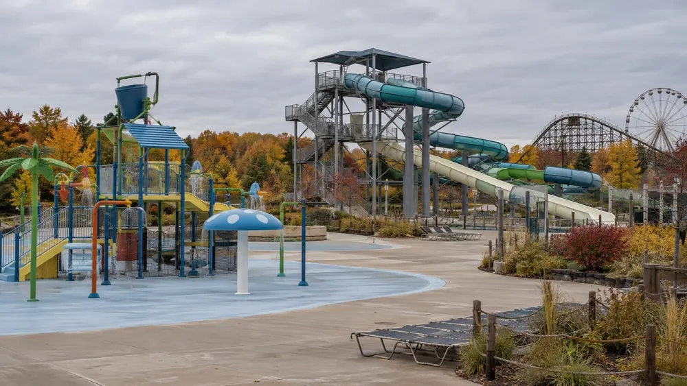 An empty outdoor waterpark with colorful slides and a family splash area surrounded by autumn foliage.