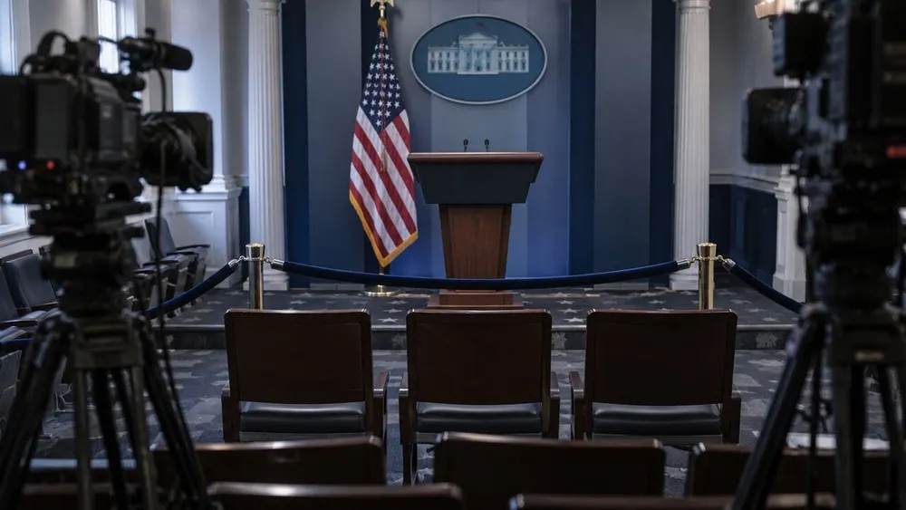 Three empty chairs behind a velvet barrier in a symbolic White House press briefing room