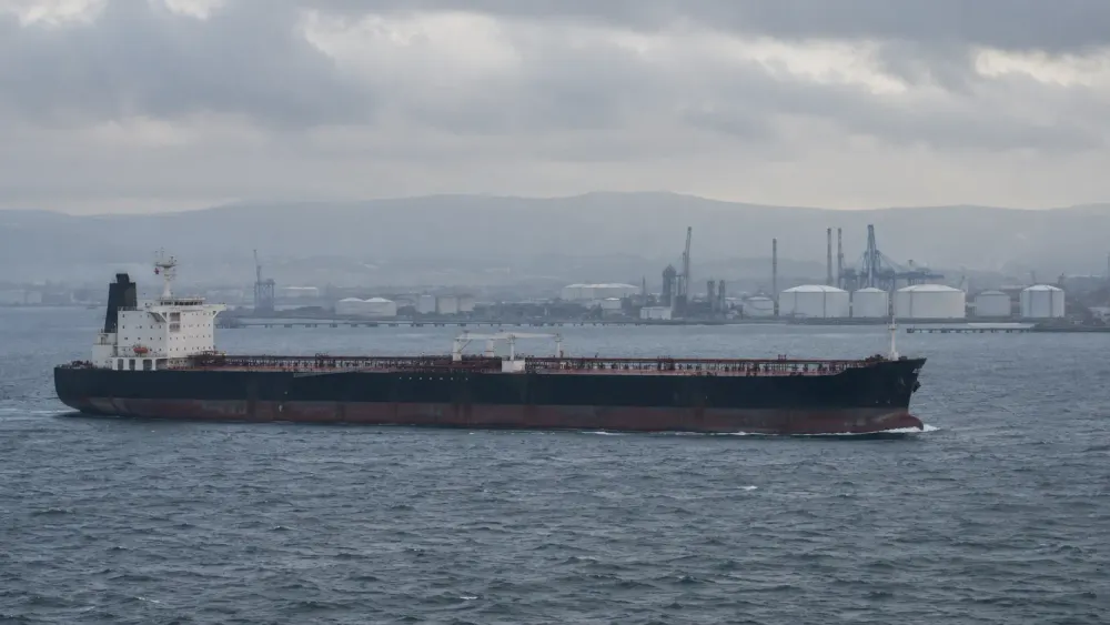 An unbranded oil tanker passes an industrial port under an overcast sky.