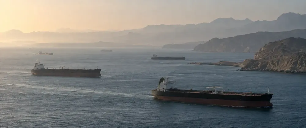 Commercial oil tankers travel through the Strait of Hormuz in subdued morning light.