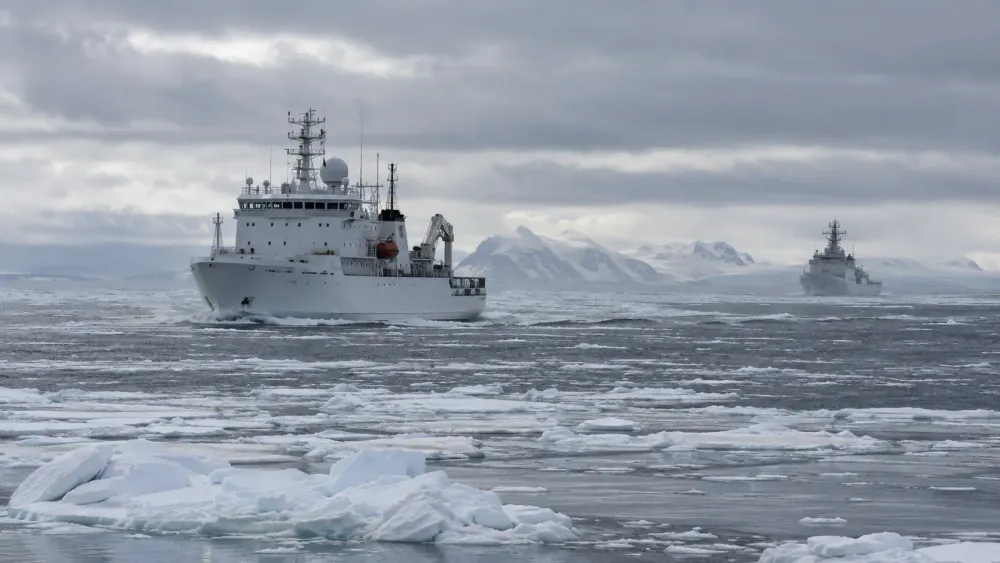 An unmarked white research ship crosses broken Arctic sea ice while a distant cutter monitors from offshore.