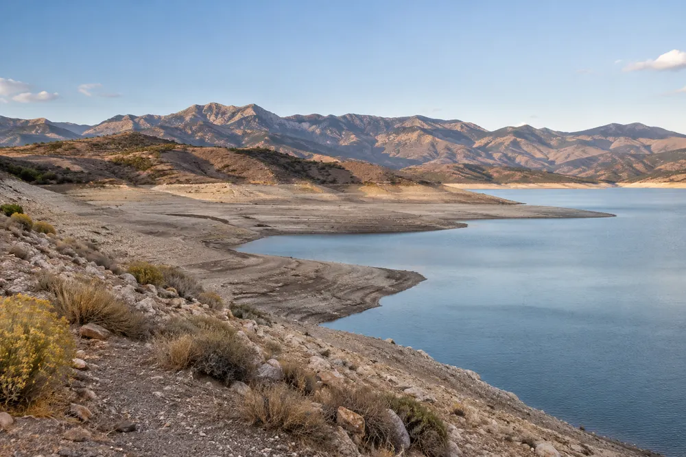 Illustrative Utah reservoir landscape with a receded shoreline, dry mountains and sparse early-autumn vegetation.