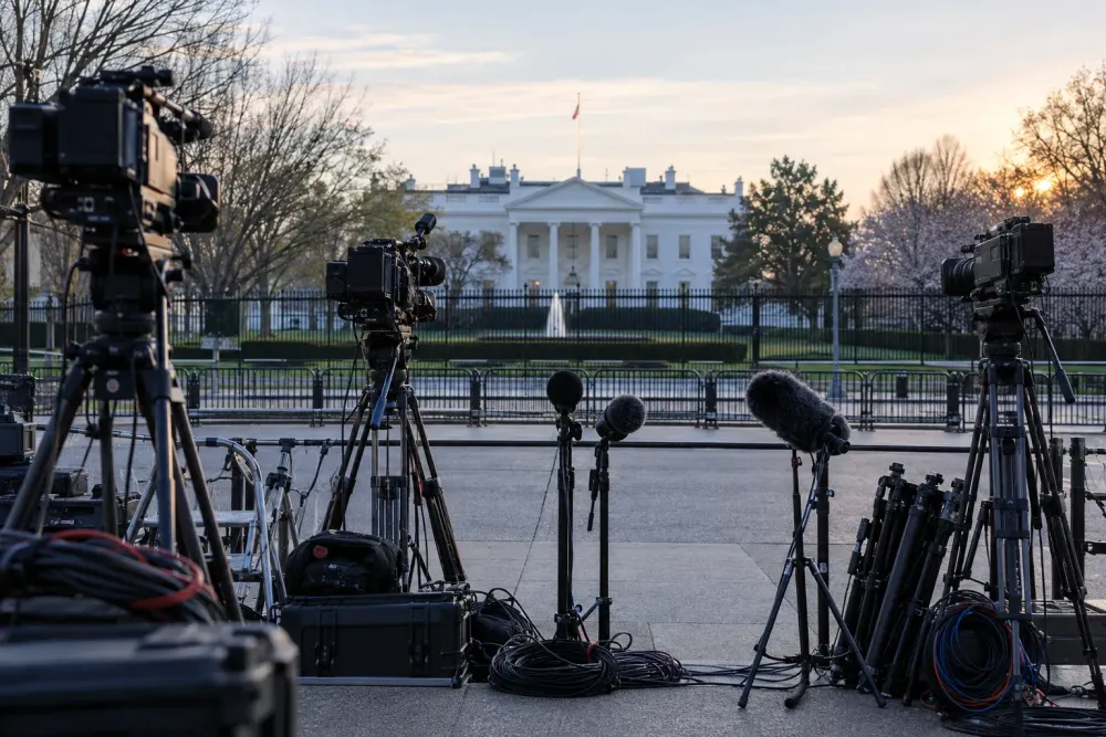 Television cameras and microphones positioned outside the White House in early morning light