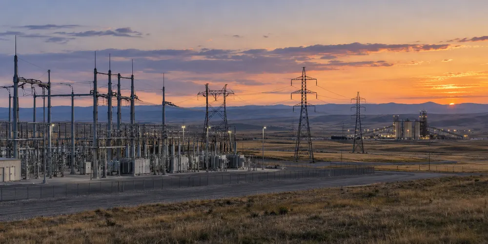 Electrical transmission lines and a modern substation stretch across the open Wyoming high plains at dusk.