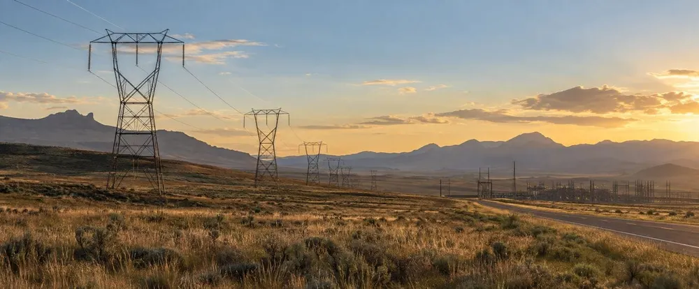 Illustration of high-voltage transmission lines crossing Wyoming rangeland near a distant substation at sunset.