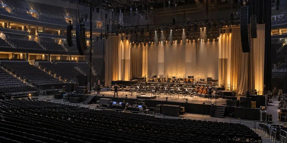Stage crews prepare a large indoor arena for a formal performing arts ceremony.