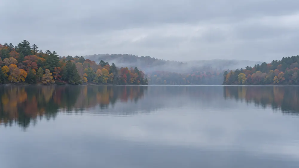 Illustrative view of a calm Rhode Island freshwater pond beneath an overcast autumn sky.