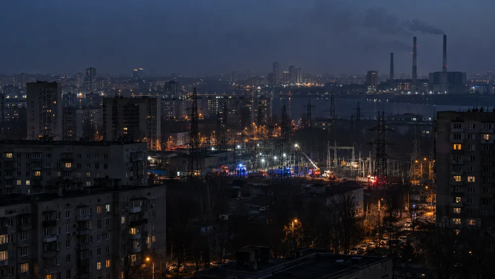 Illustrative nighttime cityscape with apartment blocks, power lines, a thermal plant and emergency vehicles near an electrical substation.