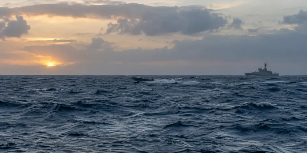 Vista ilustrativa de uma pequena lancha rápida e de um navio patrulha ao longe, no Mar das Caraíbas, ao amanhecer