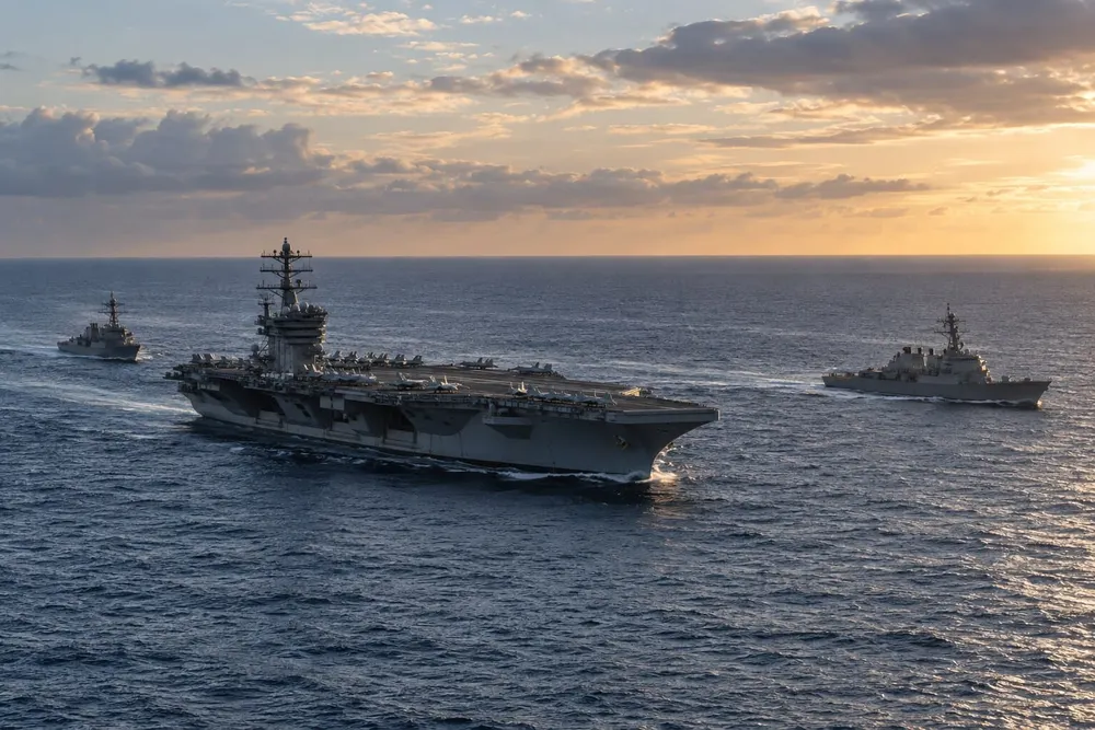 A generic aircraft carrier sailing with two escort ships on open ocean at sunset.