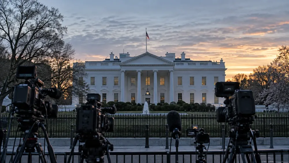 Broadcast cameras facing the White House at dawn in an illustrative editorial scene