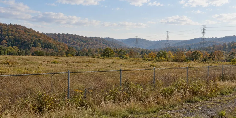 AI-generated editorial illustration of undeveloped industrial land and distant power lines; not a proposed West Virginia nuclear site or an existing nuclear facility.