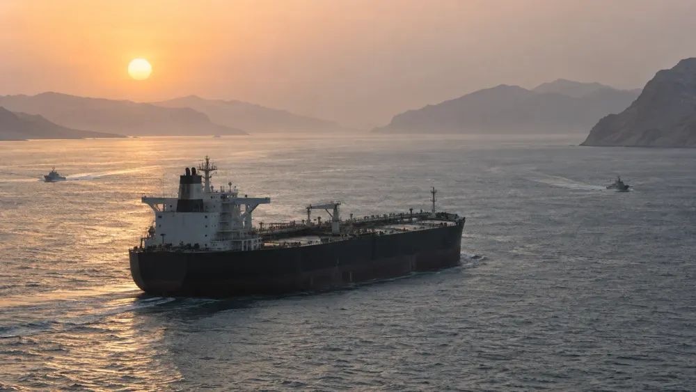 An unbranded oil tanker transiting a narrow sea lane at sunrise with two patrol craft in the distance