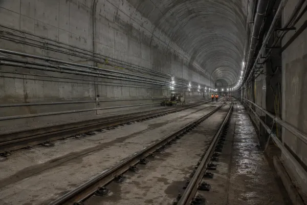An unfinished underground rail tunnel with tracks, utility conduits and distant construction workers